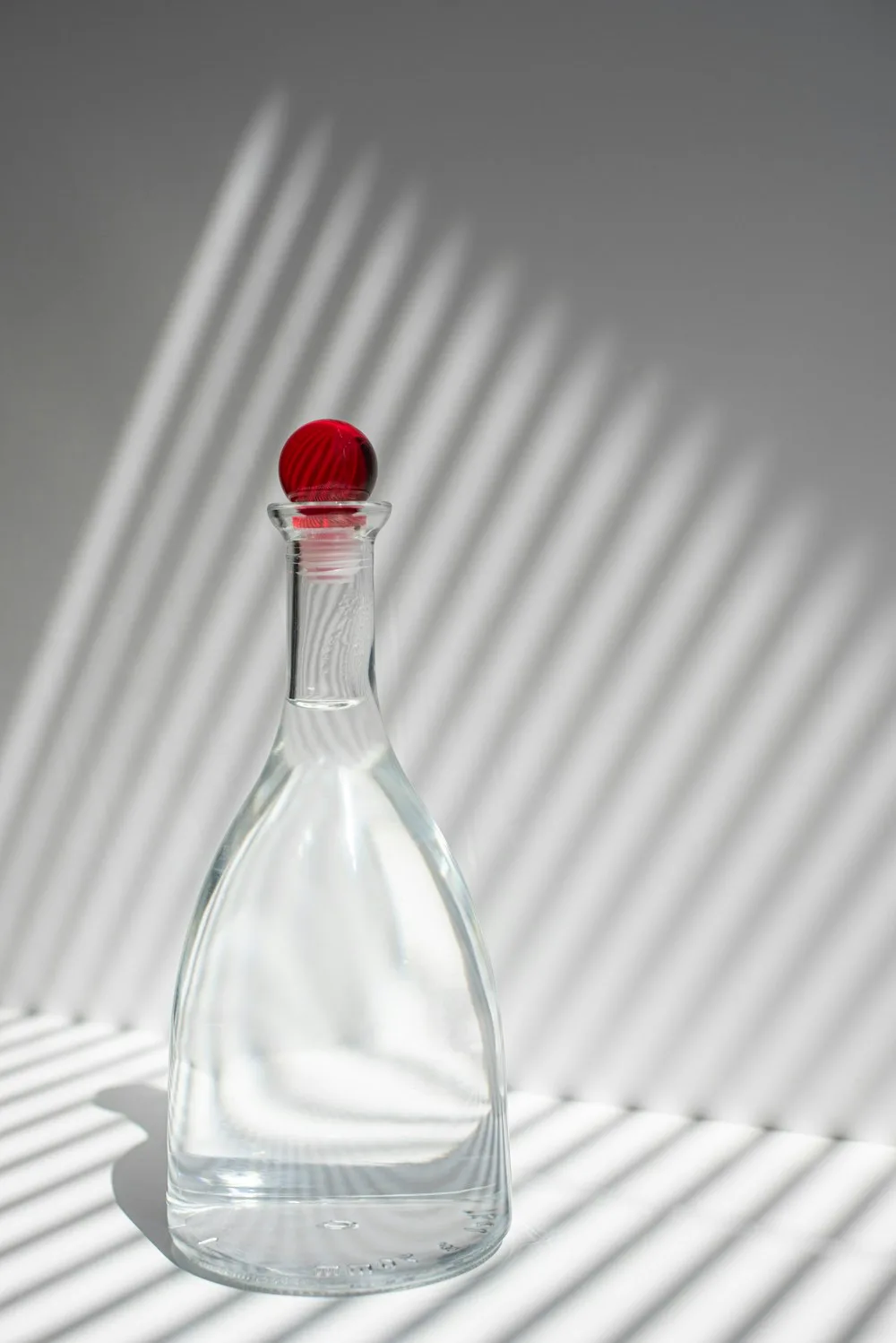 A clear glass decanter in striped shadow
